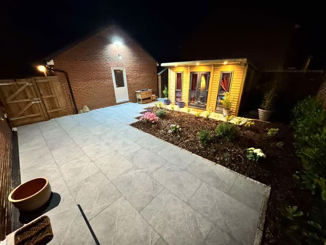 Finished garden at night with a paved terrace, planted bed and illuminated garden room