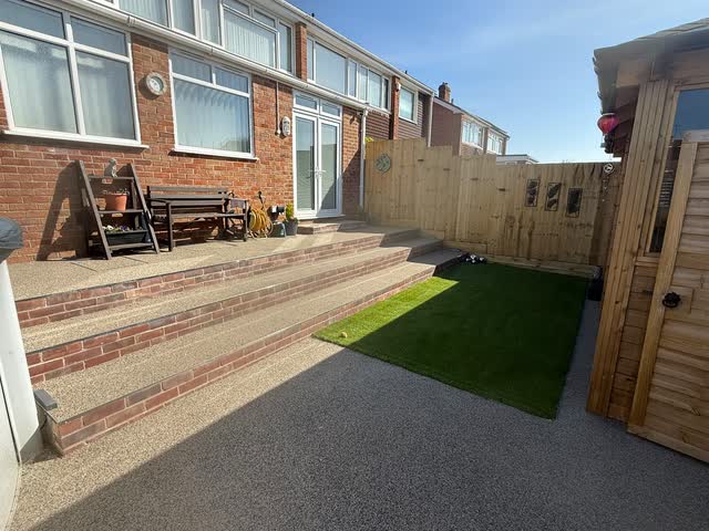 Finished garden with resin surfaces, broad steps, timber fencing and a central lawn
